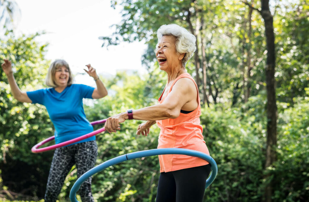 Senior women using a hula hoop to have a fun exercising time in the garden at our senior living community.