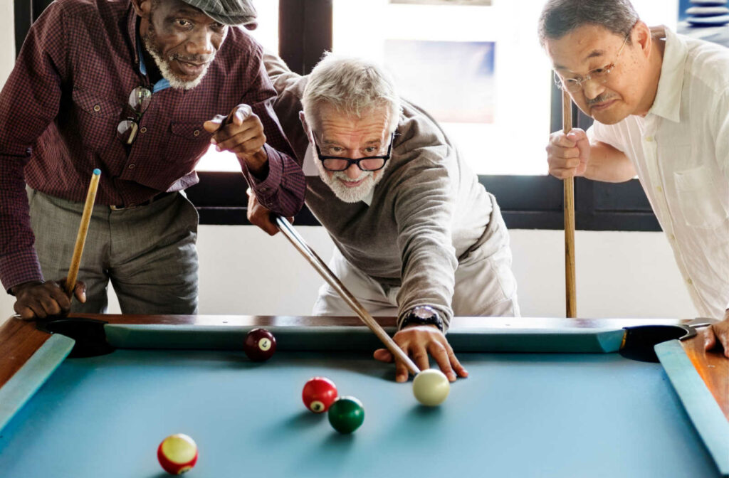 Three senior men playing a game of pool at the billiards table.